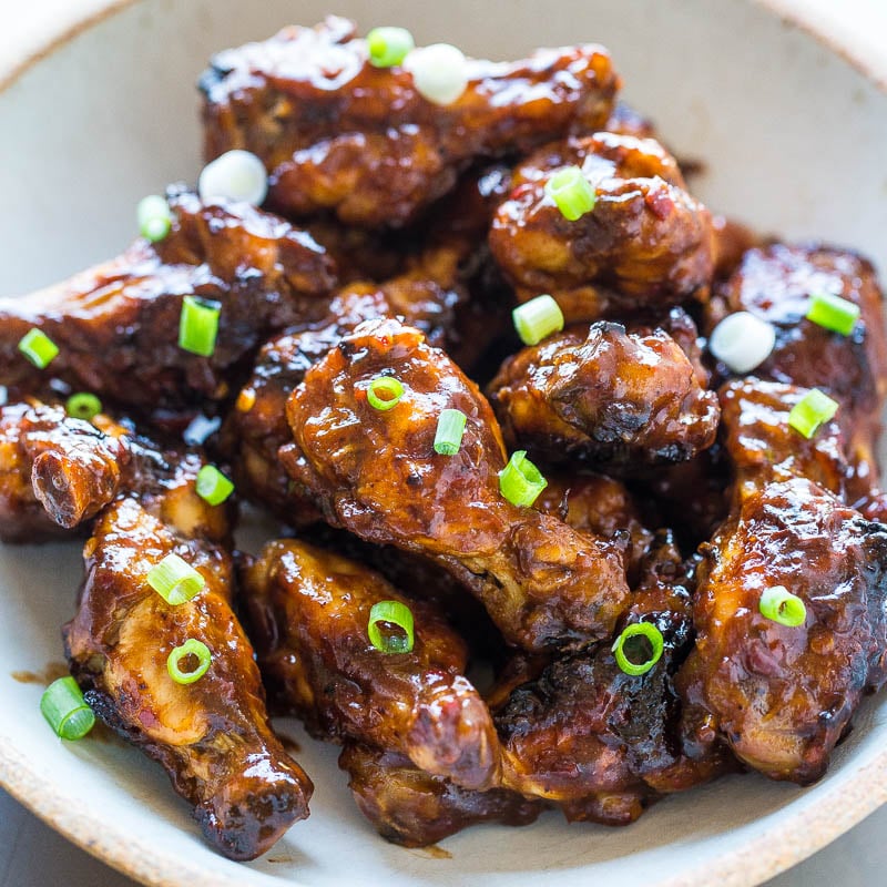 A bowl of glazed chicken wings garnished with sliced green onions.