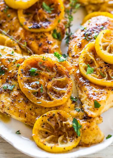 Grilled chicken breasts topped with lemon slices and herbs on a white plate.