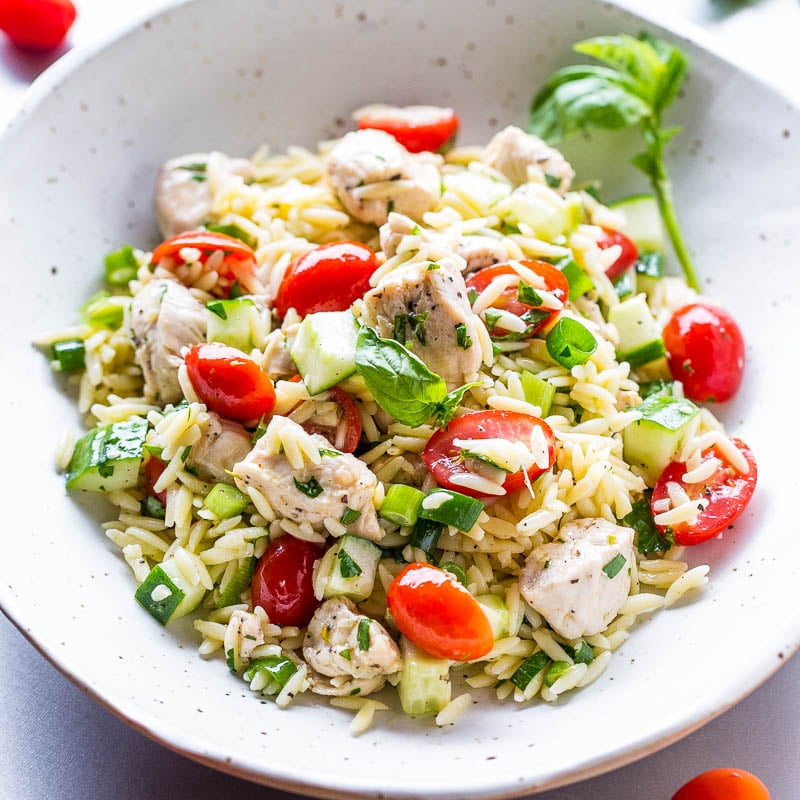A bowl of chicken and rice salad with cherry tomatoes, avocado, and basil.