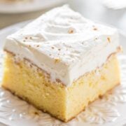 A slice of tres leches cake with whipped cream topping on a decorative plate.