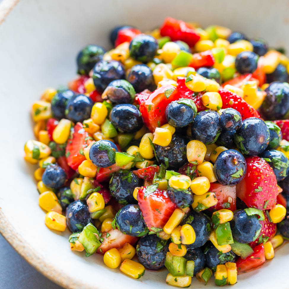 A colorful bowl of fruit and corn salad with strawberries, blueberries, corn kernels, and chopped green peppers.