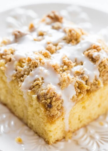 A slice of crumb cake with icing on a white plate.