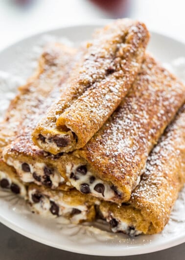 A plate of freshly made crepes filled with chocolate chips and dusted with powdered sugar.