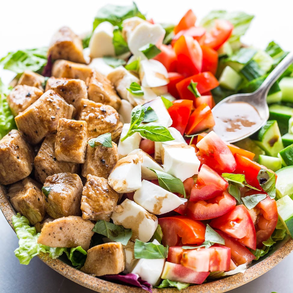 A bowl of fresh salad with tomatoes, cucumber, cheese, lettuce, and grilled tofu pieces.