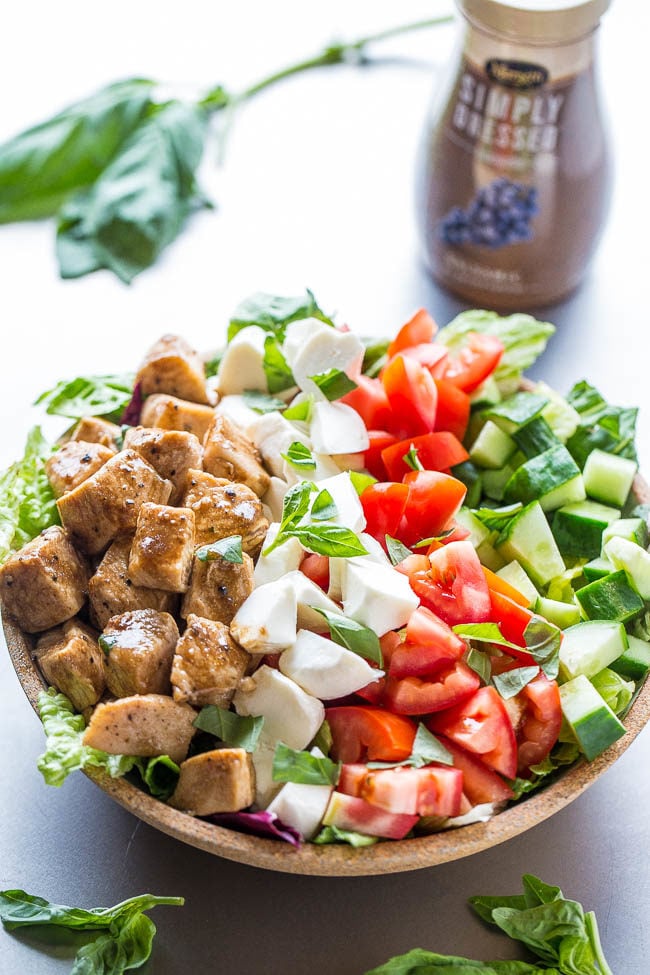 chicken caprese salad in a large bowl with a bottle of dressing in the background