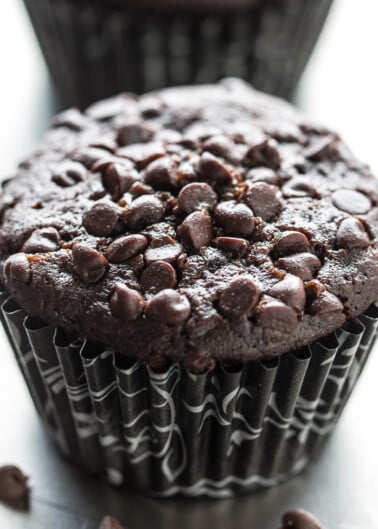 A close-up of a chocolate muffin with chocolate chips on a dark background.