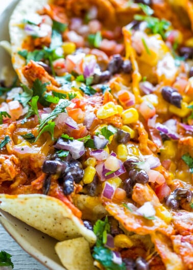 A platter of loaded nachos topped with cheese, beans, corn, chicken, and fresh pico de gallo.