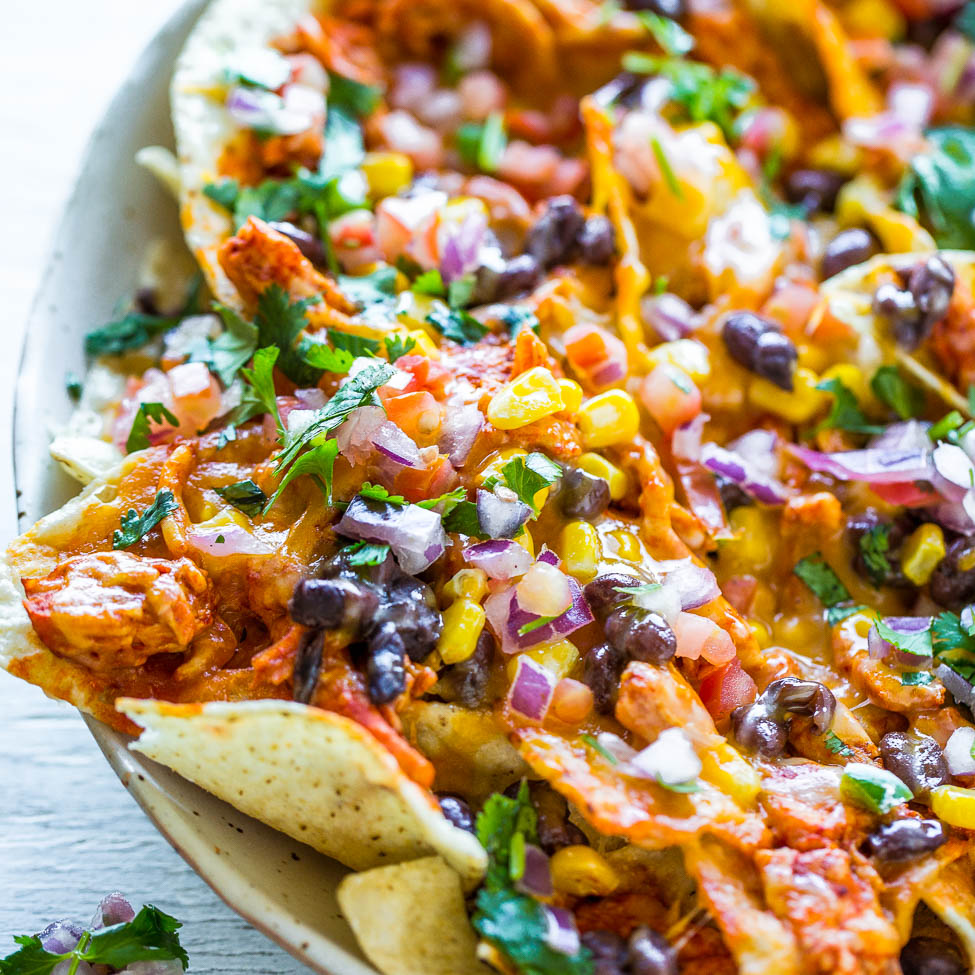 A platter of loaded nachos topped with cheese, beans, corn, chicken, and fresh pico de gallo.