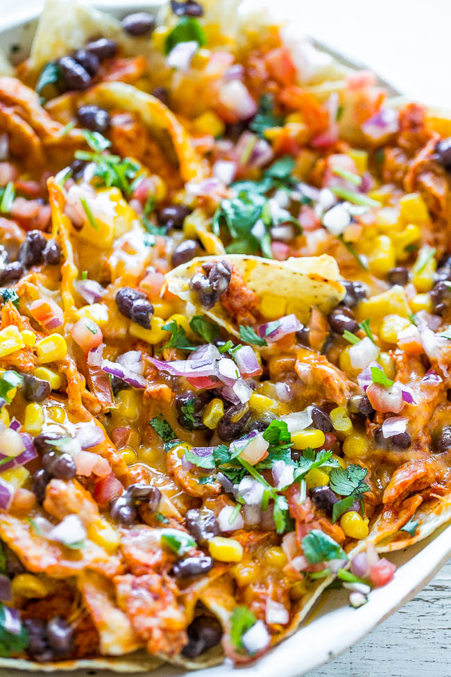 Loaded Shredded Chicken Nachos — Juicy chicken soaked in enchilada sauce with black beans, corn, peppers, cilantro, and more!! Cheesy, gooey perfection and READY in 5 minutes! Perfect for parties, tailgating, or anytime you need an EASY nacho fix!!