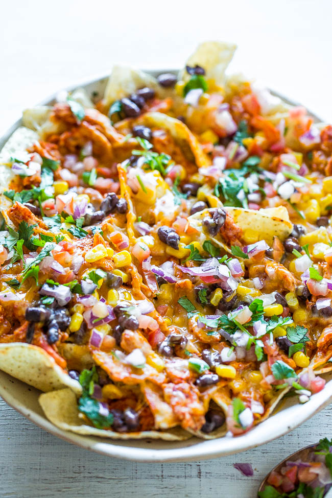 Loaded Shredded Chicken Nachos — Juicy chicken soaked in enchilada sauce with black beans, corn, peppers, cilantro, and more!! Cheesy, gooey perfection and READY in 5 minutes! Perfect for parties, tailgating, or anytime you need an EASY nacho fix!!