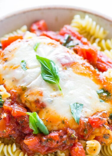A plate of chicken parmesan served over spiral pasta, topped with tomato sauce, melted cheese, and fresh basil.