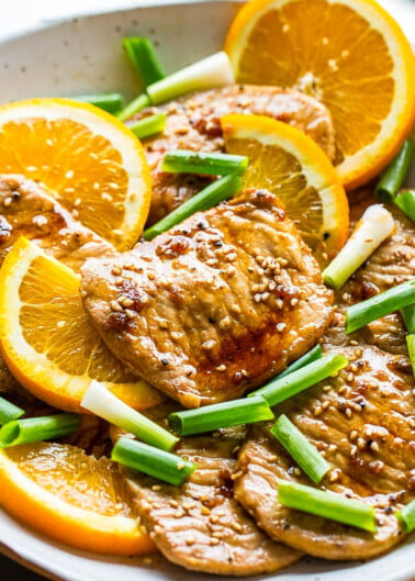 Grilled chicken with orange slices and scallions garnished with sesame seeds.