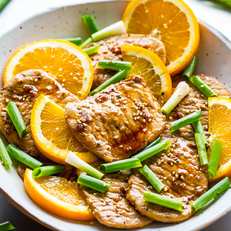 Grilled chicken with orange slices and scallions garnished with sesame seeds.