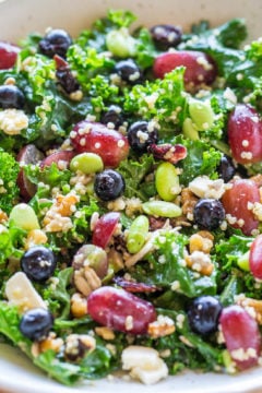 A colorful kale salad with mixed beans, seeds, and crumbled cheese.