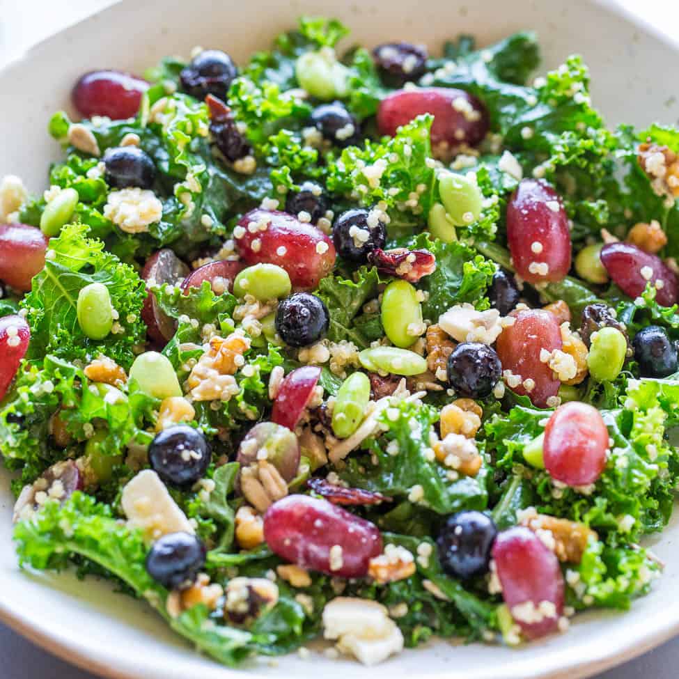 A colorful kale salad with mixed beans, seeds, and crumbled cheese.