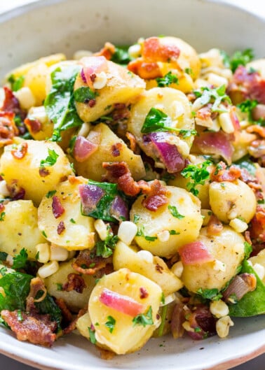 A bowl of potato salad garnished with bacon, herbs, and corn.