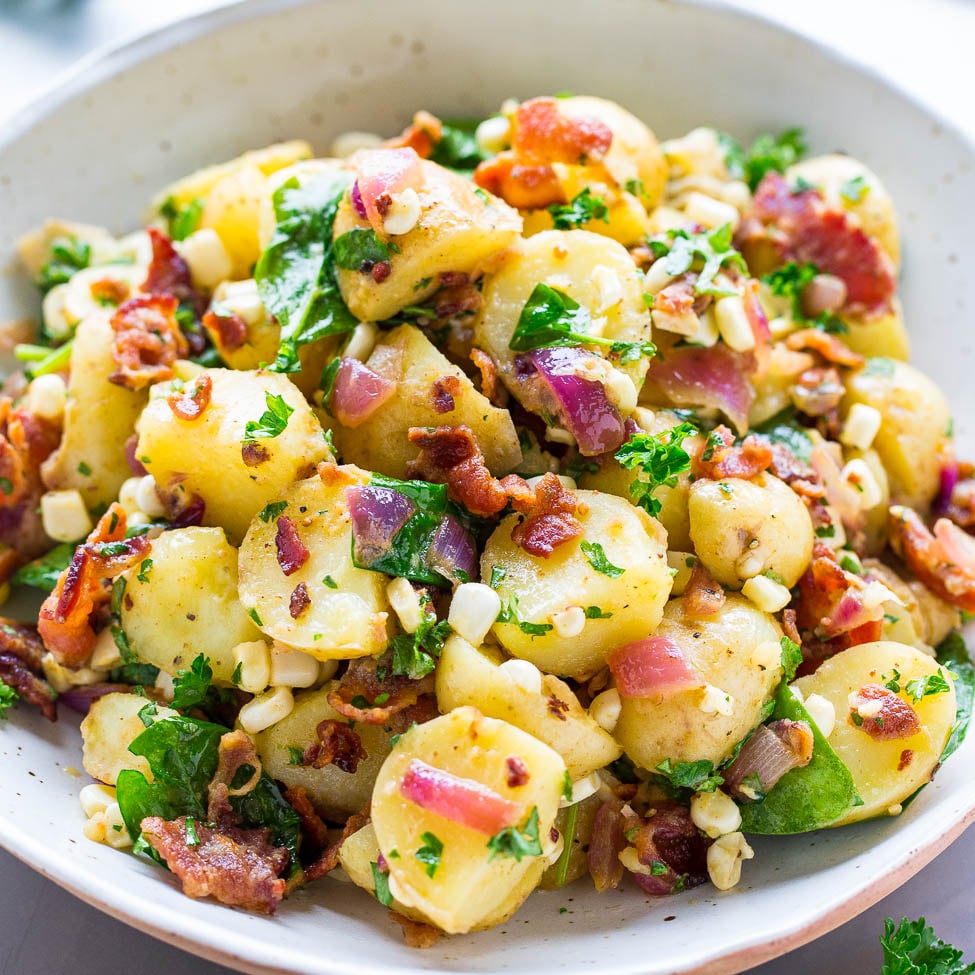 A bowl of potato salad garnished with bacon, herbs, and corn.
