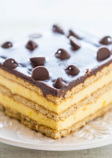 A slice of layered dessert with chocolate frosting and chocolate chips on a white plate.
