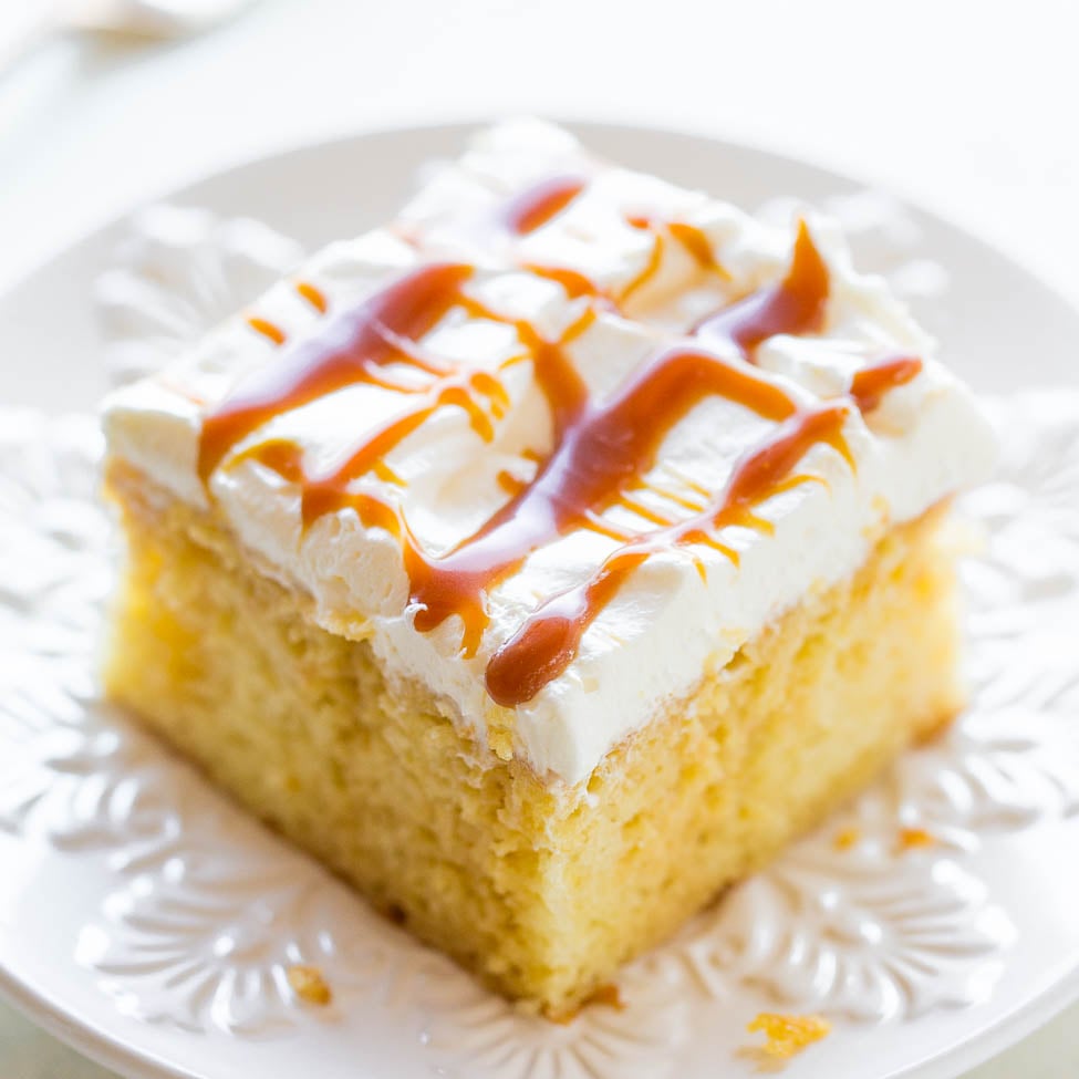 A slice of caramel drizzled cake with whipped cream topping on a white plate.