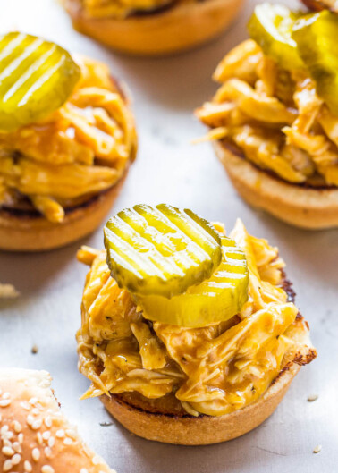 A close-up of pulled chicken sandwiches topped with pickles on sesame-seed buns.