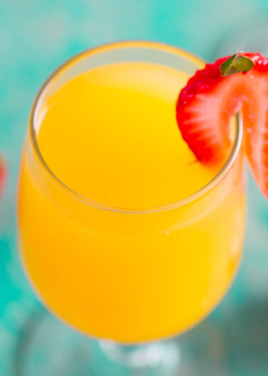 A glass of orange juice with a sliced strawberry on the rim.