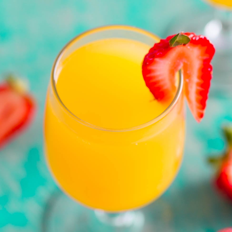 A glass of orange juice with a sliced strawberry on the rim.