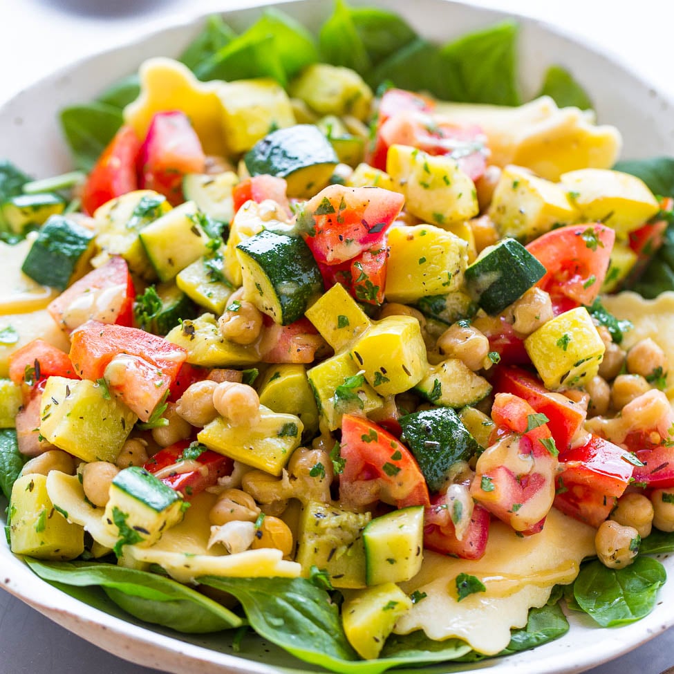 A bowl of colorful salad with chickpeas, avocado, tomatoes, cucumber, and spinach leaves.