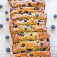 Sliced blueberry loaf cake with fresh blueberries scattered around on a wooden surface.