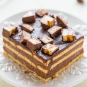 A chocolate layer cake topped with pieces of chocolate bar on a white plate.