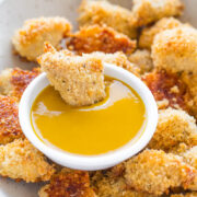 Breaded chicken pieces surrounding a bowl of honey mustard sauce.
