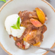 A bowl of fruit cobbler topped with a scoop of vanilla ice cream and a mint leaf.