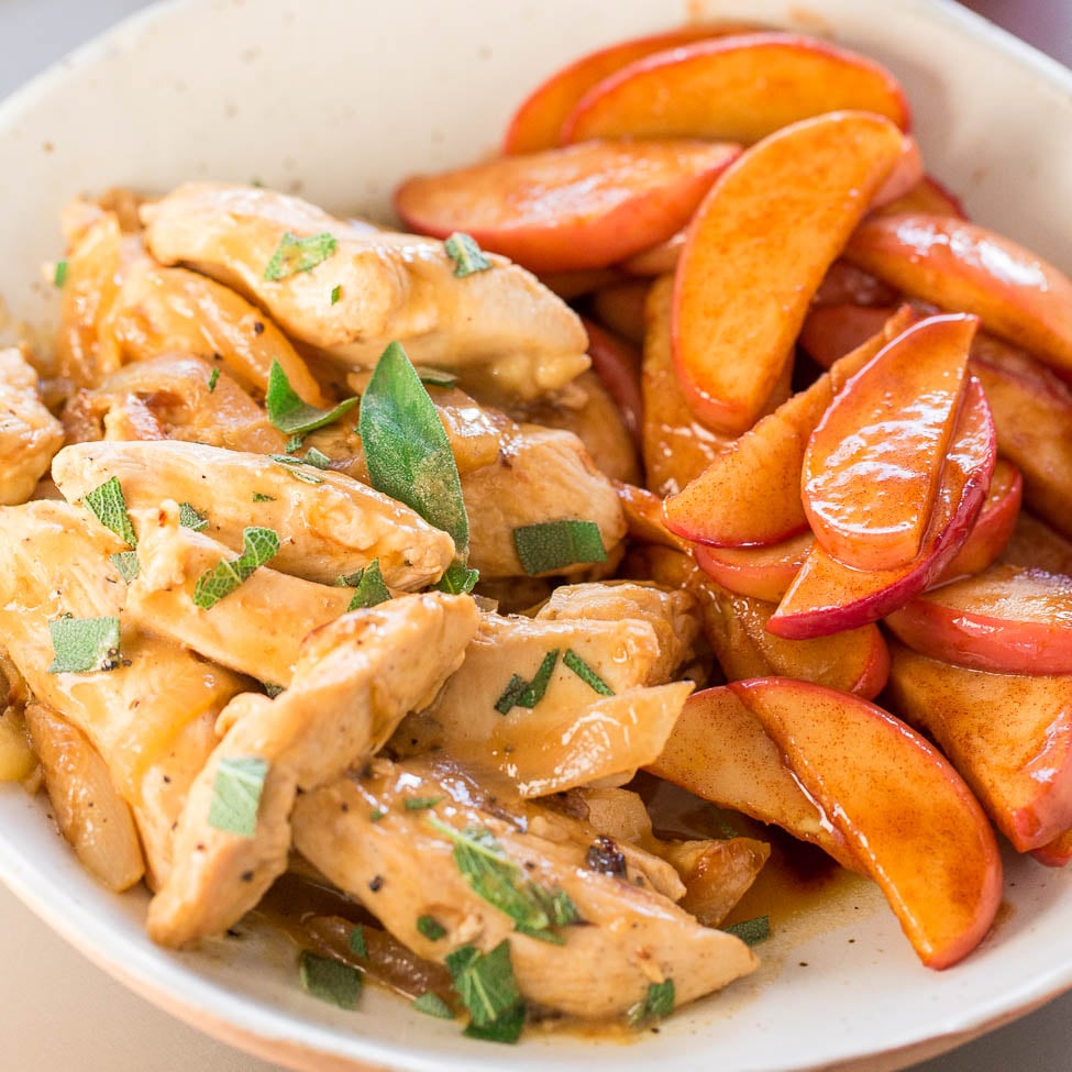 A bowl containing chicken strips and sautéed apple slices garnished with herbs.