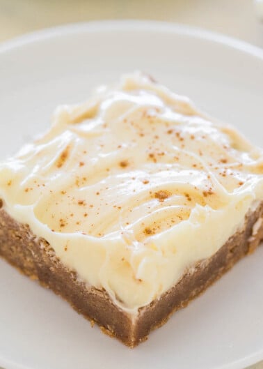 A slice of cheesecake with a graham cracker crust, topped with cream and a sprinkle of cinnamon.