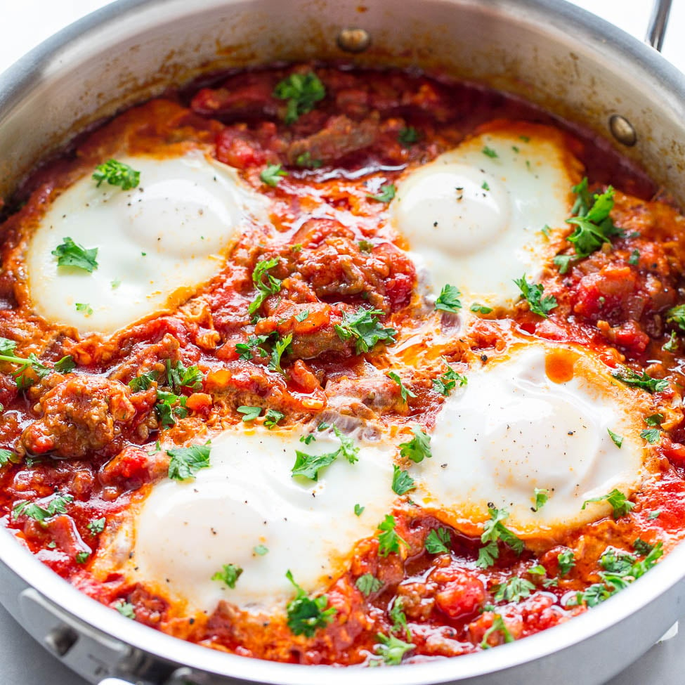 A skillet containing shakshuka, a dish of poached eggs in a tomato and pepper sauce garnished with fresh herbs.