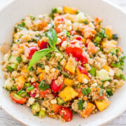 A bowl of quinoa salad with tomatoes, corn, cucumbers, and herbs.