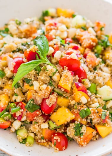A bowl of quinoa salad with tomatoes, corn, cucumbers, and herbs.