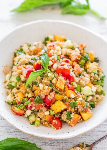 A bowl of quinoa salad with mango, tomatoes, cucumbers, and fresh herbs.
