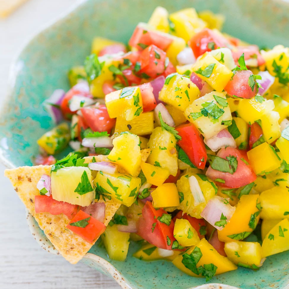 A colorful bowl of mango salsa with a tortilla chip.