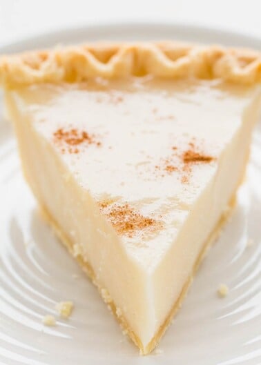 A slice of custard pie topped with a dusting of cinnamon on a white plate.