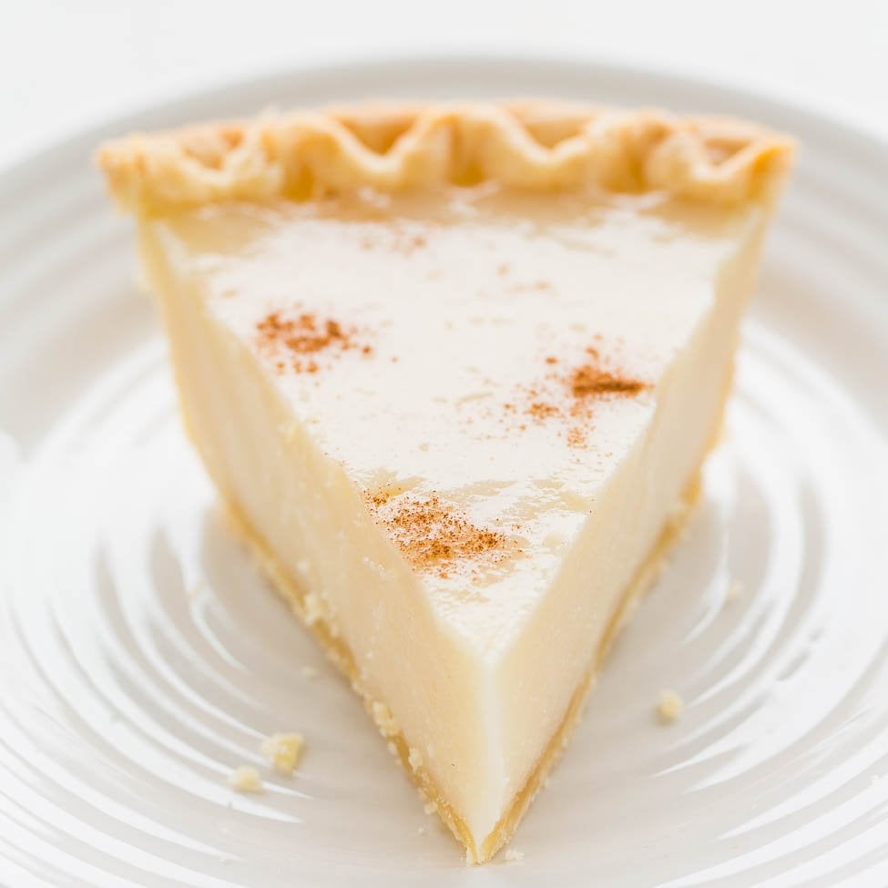 A slice of custard pie topped with a dusting of cinnamon on a white plate.