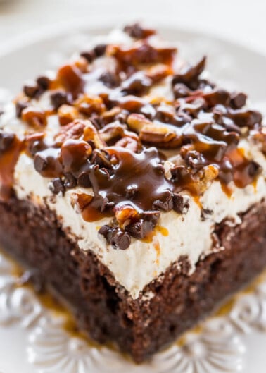 A piece of chocolate cake topped with whipped cream, drizzled with chocolate sauce, and sprinkled with chopped nuts.