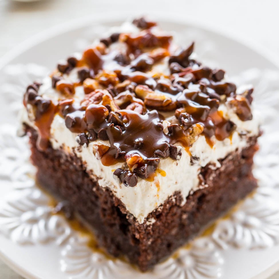 A piece of chocolate cake topped with whipped cream, drizzled with chocolate sauce, and sprinkled with chopped nuts.