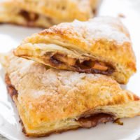 Freshly baked apple turnovers sprinkled with sugar on a white plate.
