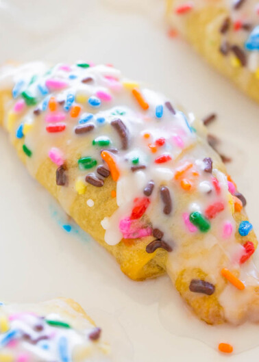 A freshly glazed scone topped with colorful sprinkles on a white plate.