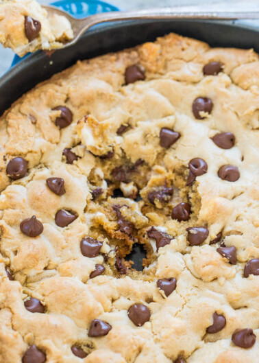 A freshly baked chocolate chip cookie skillet with a slice being lifted out.