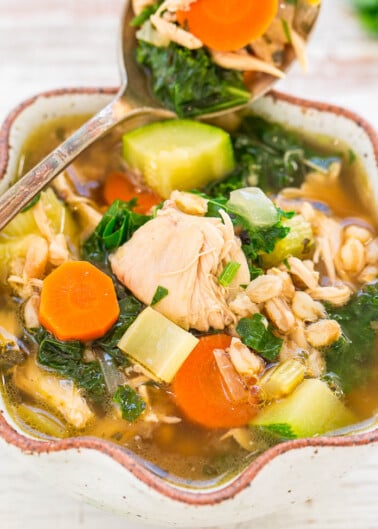 A bowl of chicken and vegetable soup with a spoon.