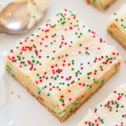 A frosted sugar cookie bar topped with colorful sprinkles on a white plate.