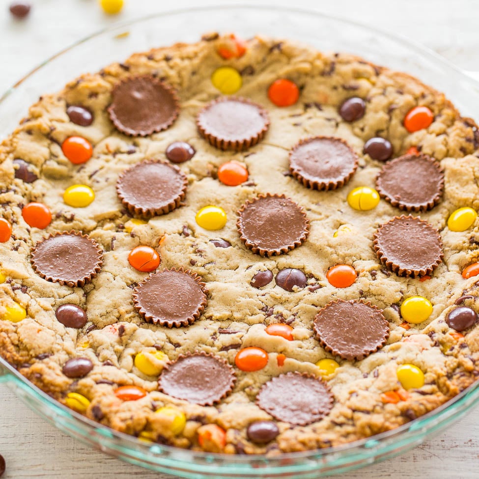 A freshly baked cookie pie with colorful candies and chocolate peanut butter cups embedded on top.