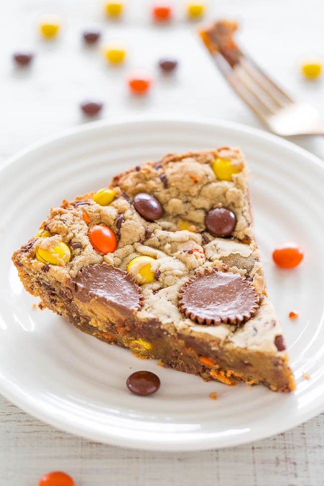 a slice of peanut butter cookie cake on a white plate with Reese's Pieces scattered around it