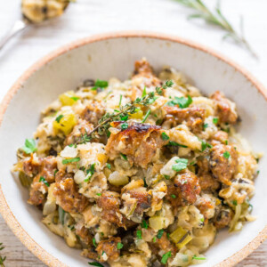 A bowl of stuffing garnished with fresh herbs on a wooden surface.